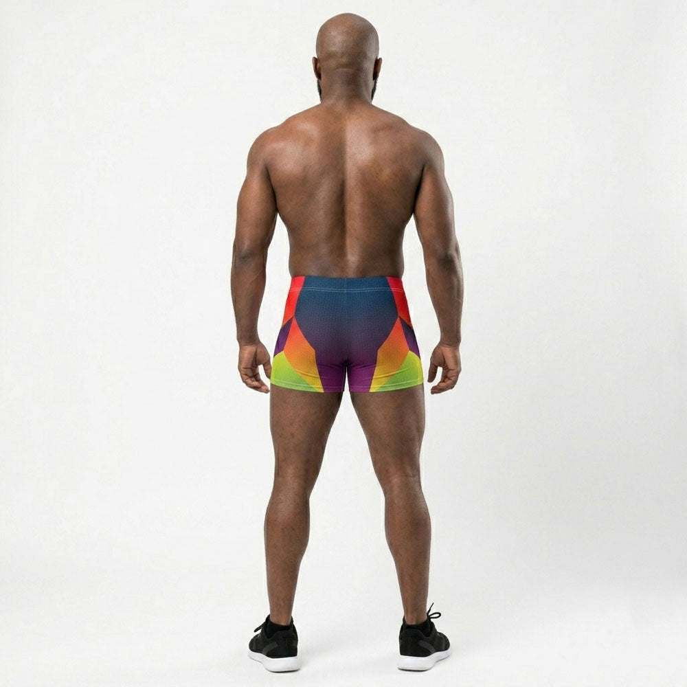 Muscular model wearing LED Queens Hypertrophy Spandex Shorts with bold geometric chevrons in red, orange, yellow-green, and lime on a navy-to-purple gradient base
