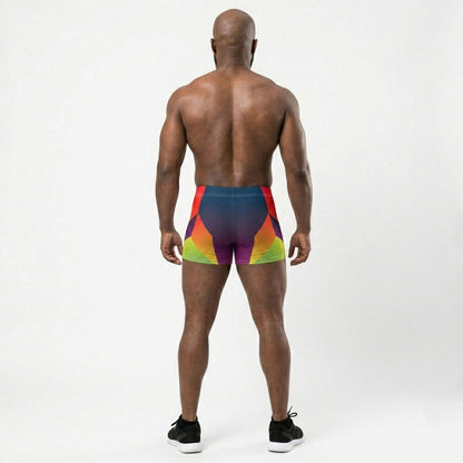 Muscular model wearing LED Queens Hypertrophy Spandex Shorts with bold geometric chevrons in red, orange, yellow-green, and lime on a navy-to-purple gradient base